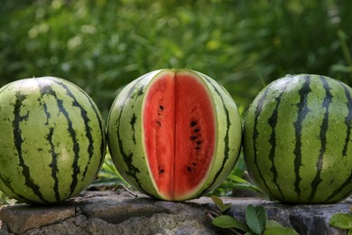 Delicious whole and cut watermelons on stone surface outdoors