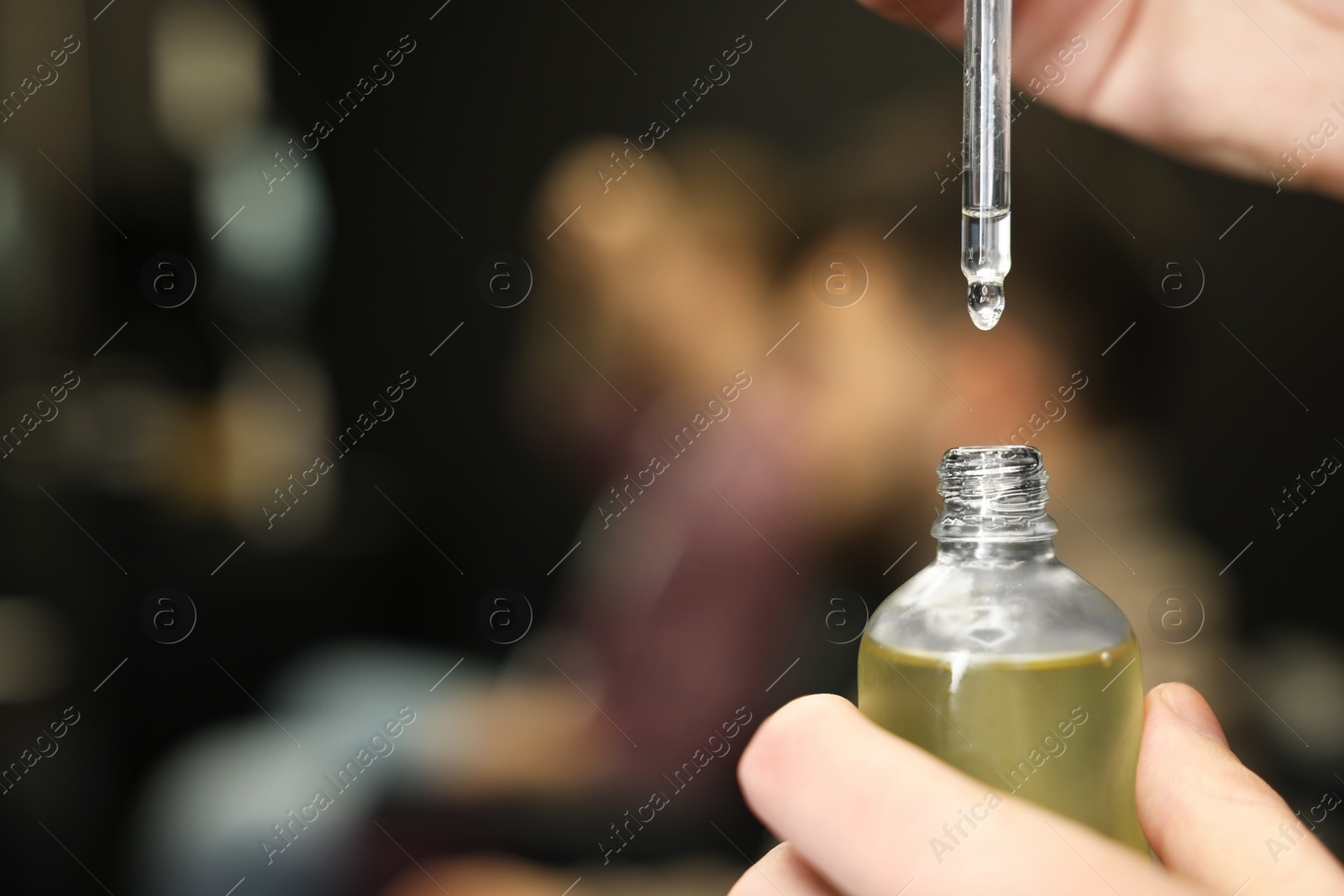 Photo of Hairdresser holding bottle of beard oil in barbershop, closeup with space for text. Professional shaving service