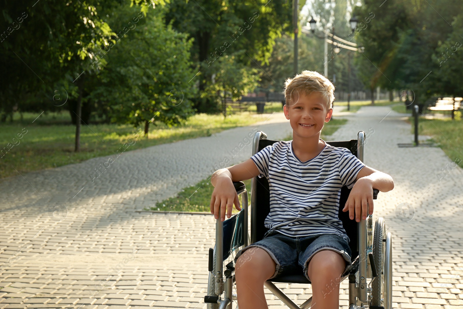 Photo of Happy little boy in wheelchair at park on sunny day. Space for text