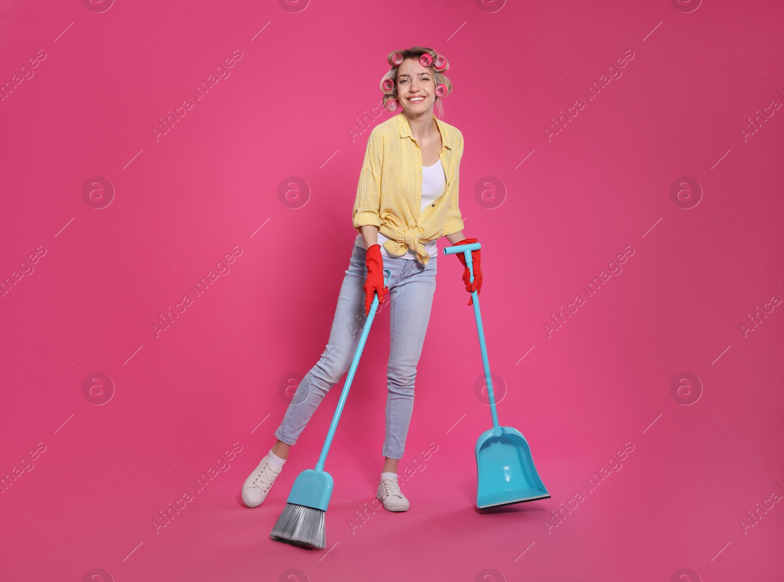 Photo of Young housewife with broom and dustpan on pink background