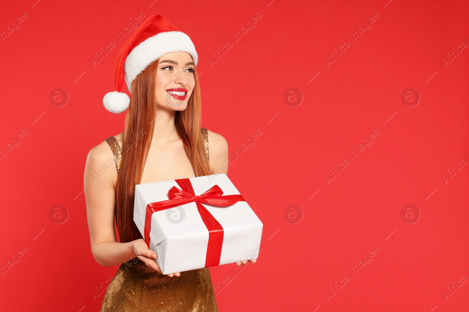 Photo of Young woman in Santa hat with Christmas gift on red background, space for text