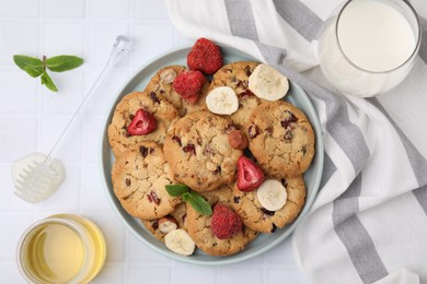 Photo of Cookies with freeze dried fruits, mint, milk, honey and nuts on white tiled table, flat lay