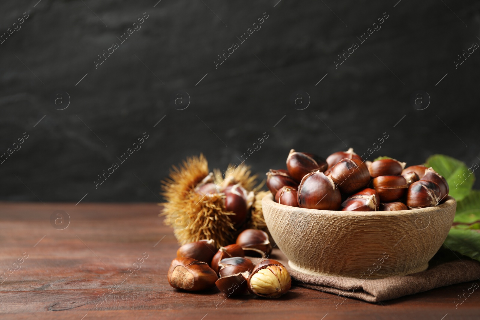 Photo of Delicious roasted edible chestnuts in bowl on wooden brown table. Space for text