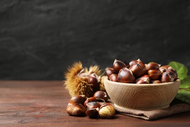 Photo of Delicious roasted edible chestnuts in bowl on wooden brown table. Space for text