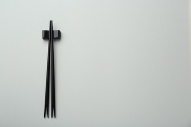 Photo of Pair of black chopsticks with rest on light grey background, top view. Space for text