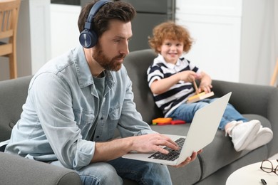 Photo of Father working remotely on laptop while his son playing with toys at home
