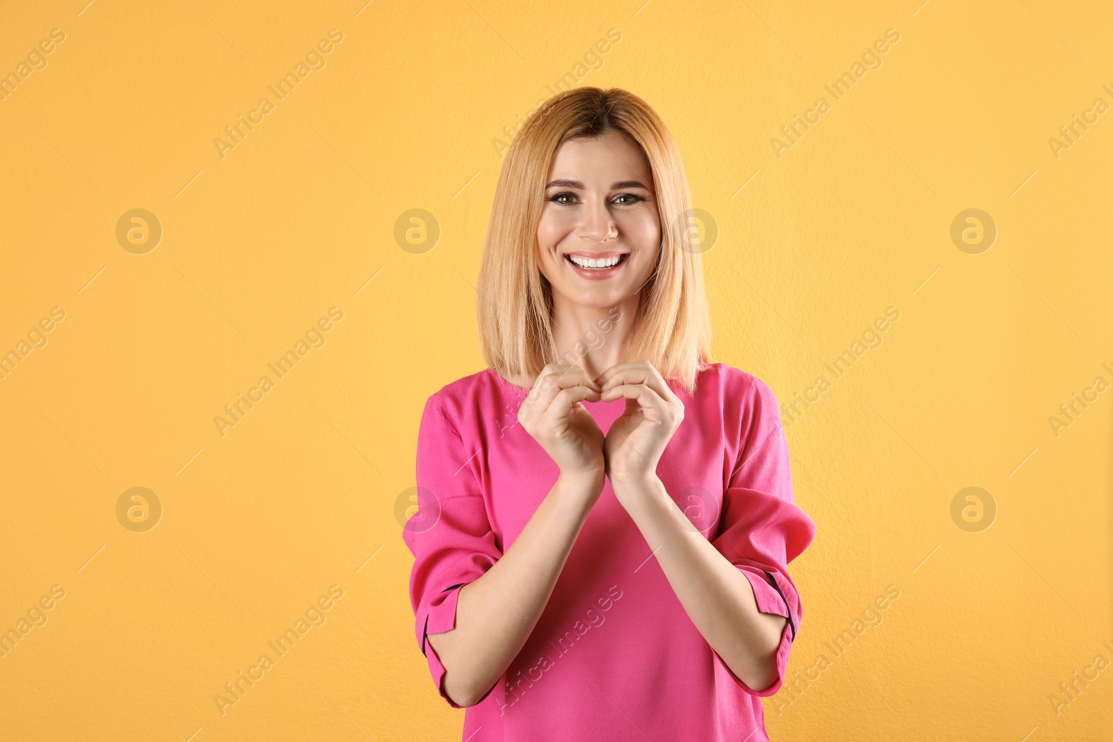 Photo of Portrait of woman making heart with her hands on color background