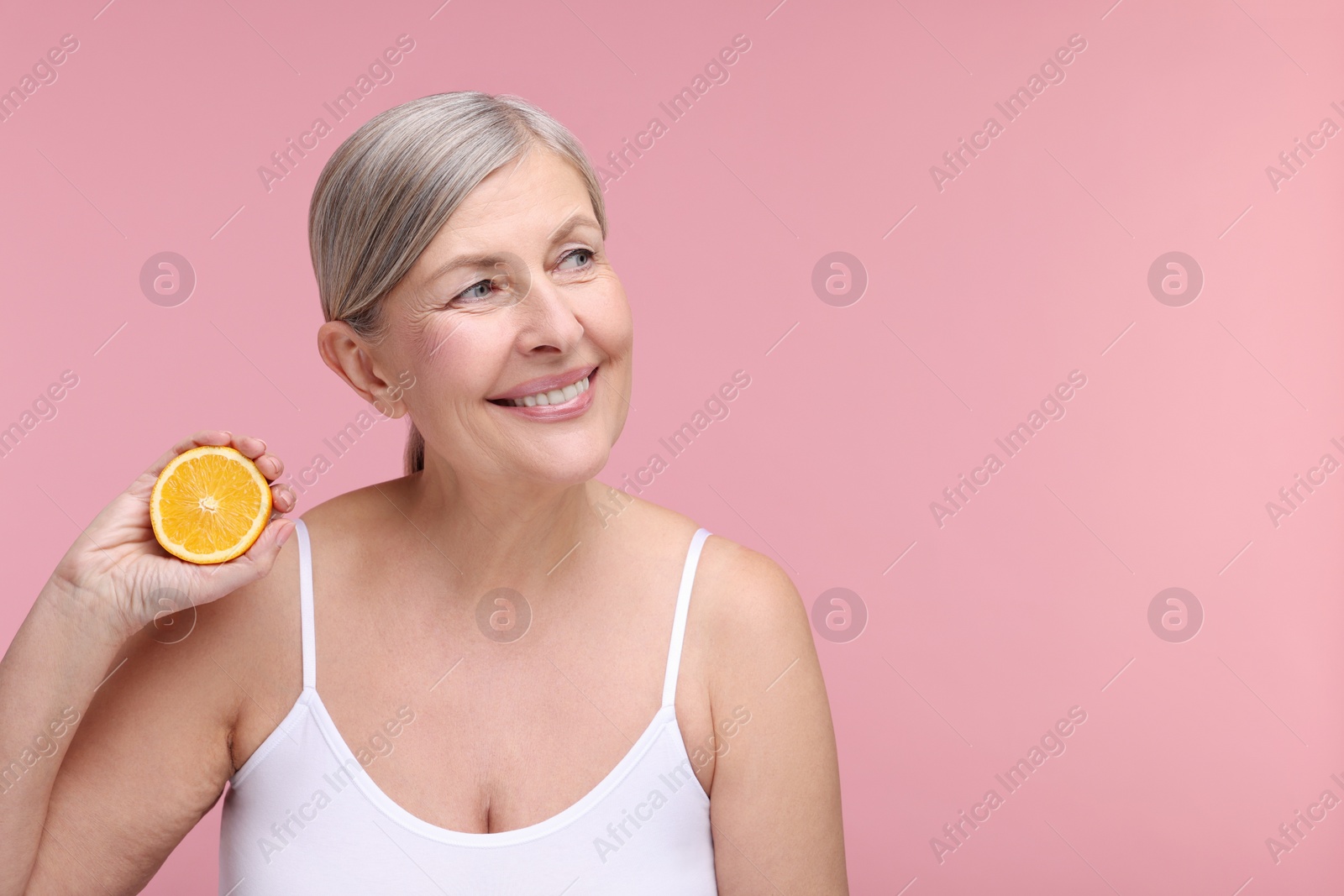 Photo of Beautiful woman with half of orange rich in vitamin C on pink background, space for text