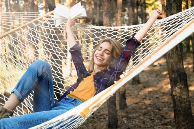 Photo of Beautiful young woman with book relaxing in hammock outdoors on summer day