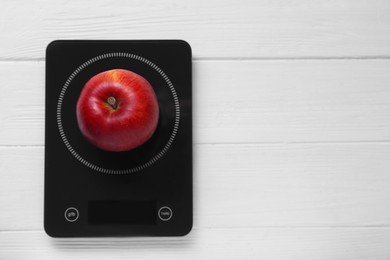 Photo of Digital kitchen scale with ripe red apple on white wooden table, top view. Space for text