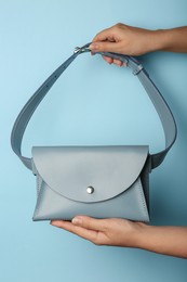 Woman holding stylish bag on light blue background, closeup