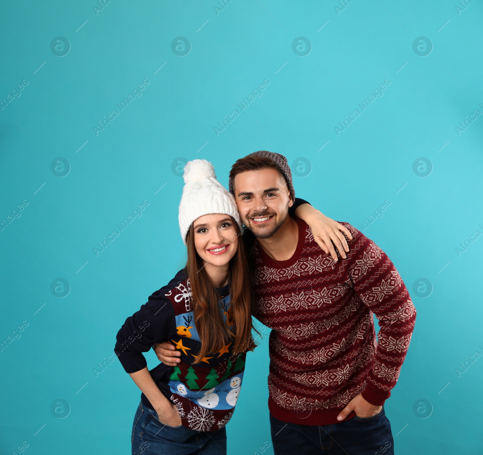 Photo of Couple wearing Christmas sweaters and hats on blue background