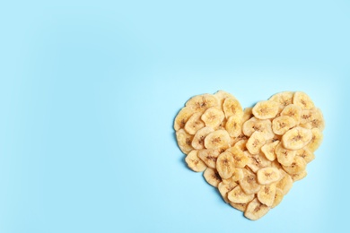 Photo of Heart shaped heap of sweet banana slices on color background, top view with space for text. Dried fruit as healthy snack