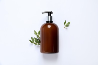 Bottle of cosmetic product and green leaves on white background, flat lay