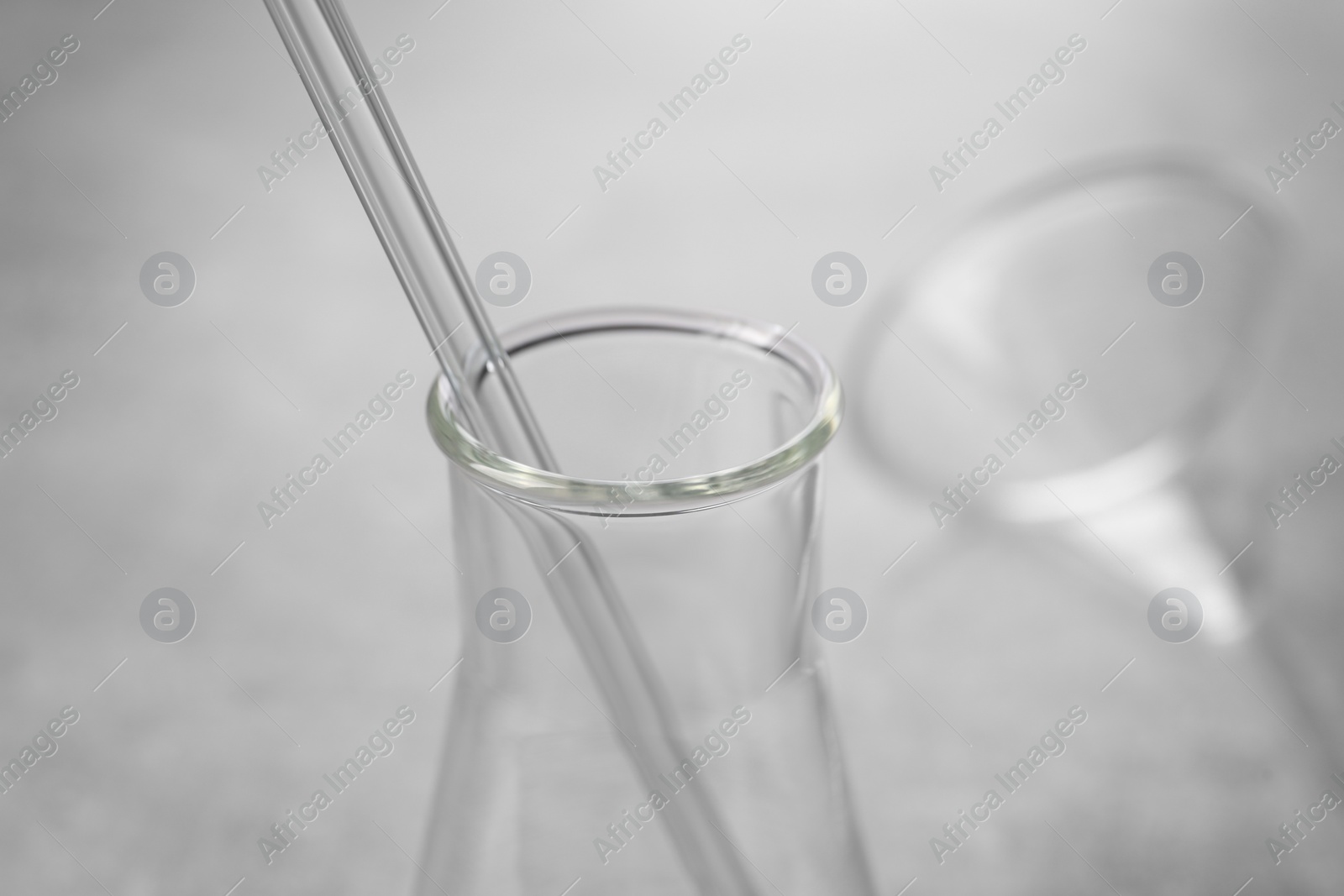 Photo of Laboratory flask with pipette on blurred background, closeup