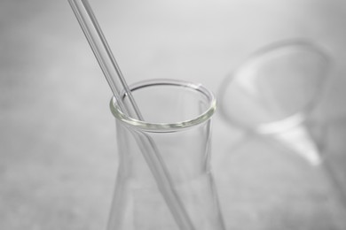 Photo of Laboratory flask with pipette on blurred background, closeup