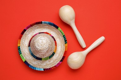 Photo of Wooden maracas and sombrero hat on red background, flat lay. Musical instrument