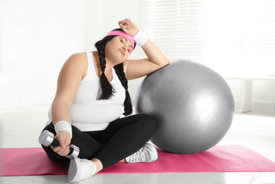 Lazy overweight woman with fit ball and dumbbell at gym