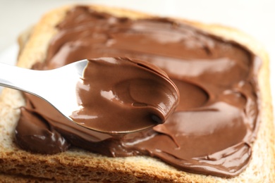 Photo of Spreading sweet chocolate cream onto toast with spoon, closeup