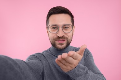 Man taking selfie and blowing kiss on pink background