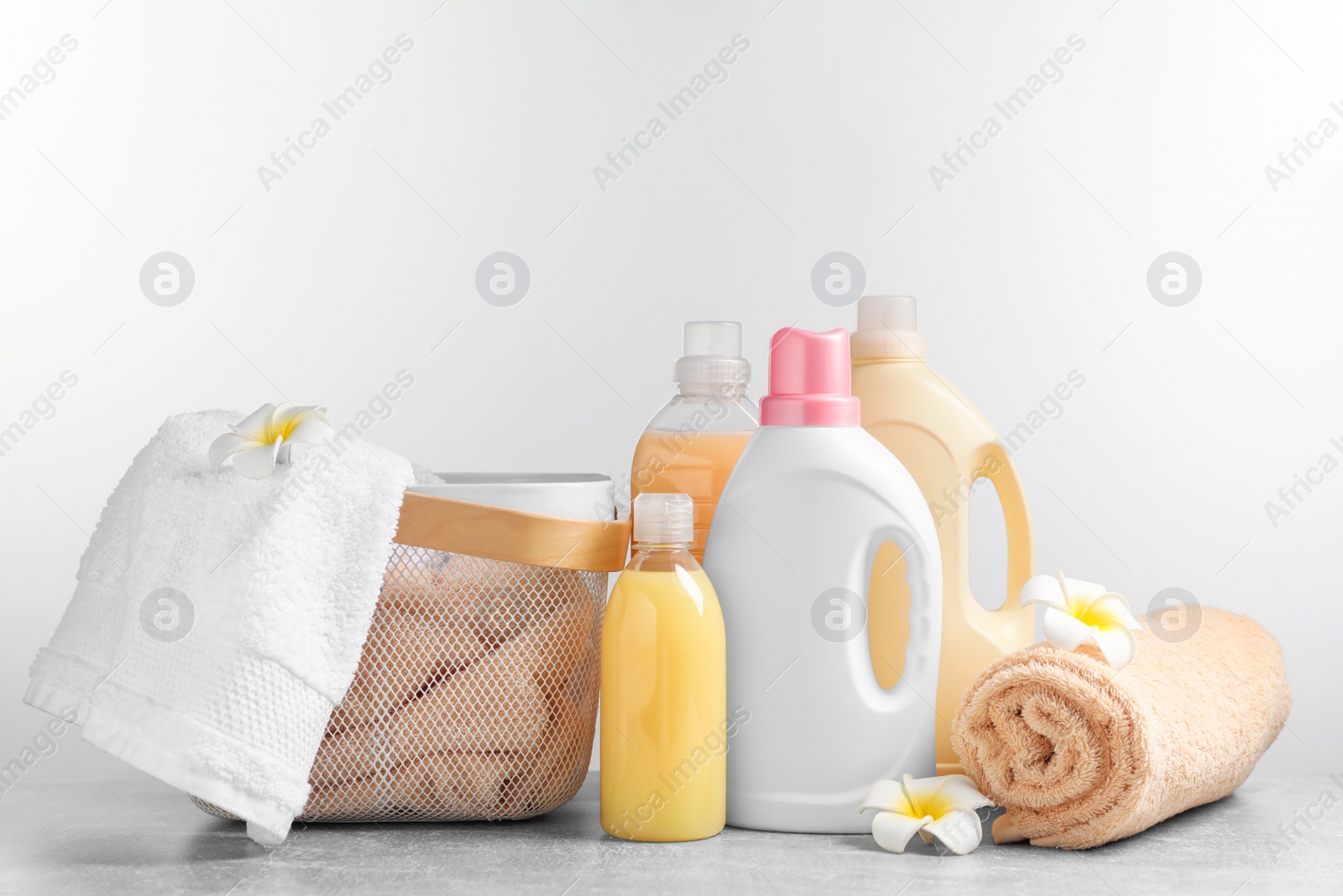 Photo of Bottles of laundry detergents and fresh towels on grey table against white background