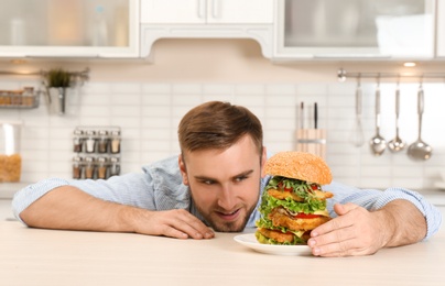 Young hungry man and huge burger on table