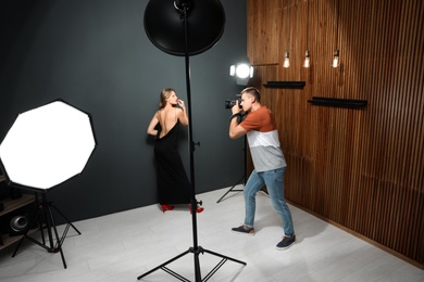 Professional photographer taking picture of young woman in modern studio