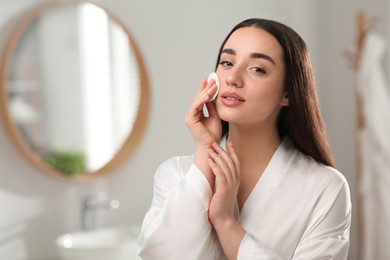 Photo of Beautiful woman removing makeup with cotton pad indoors