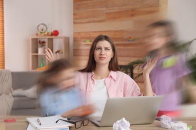 Image of Children disturbing overwhelmed woman in living room. Working from home during quarantine