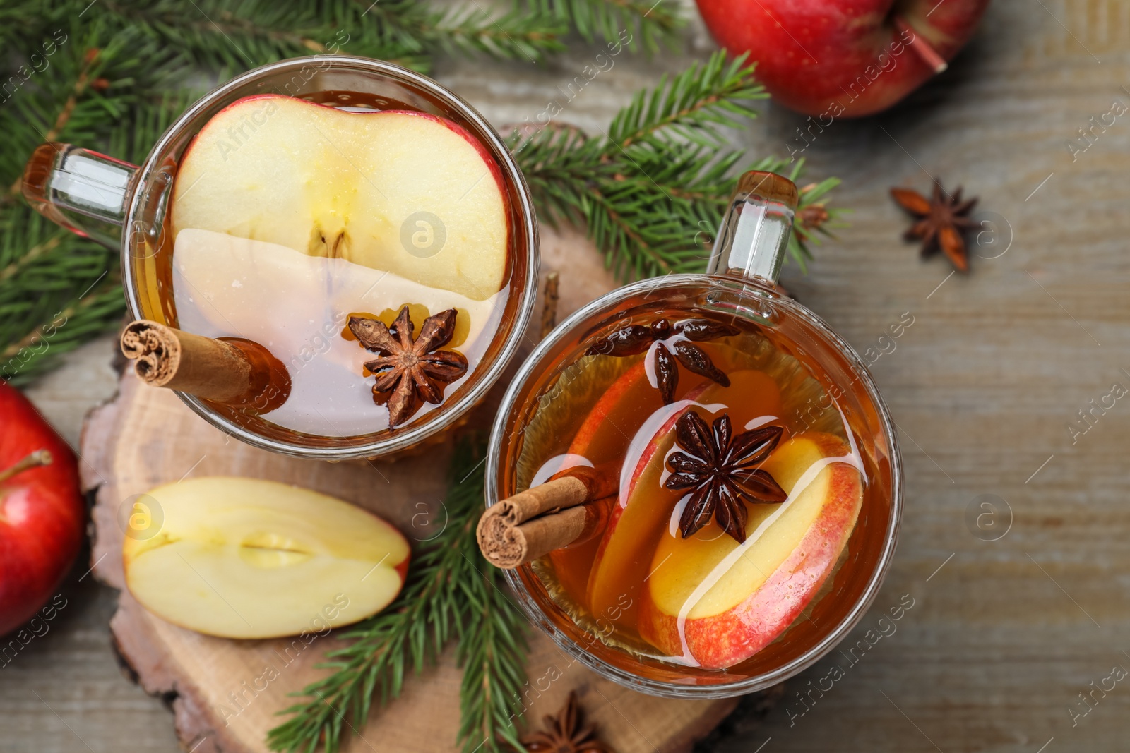 Photo of Hot mulled cider, fresh fruits and fir branches on wooden table, flat lay