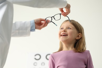 Vision testing. Ophthalmologist giving glasses to little girl indoors, low angle view
