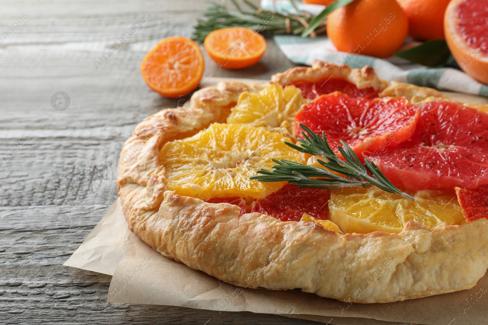 Photo of Delicious galette with citrus fruits and rosemary on wooden table, closeup