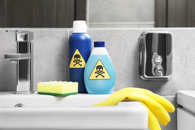 Photo of Bottles of toxic household chemicals with warning signs, gloves and scouring sponge in bathroom