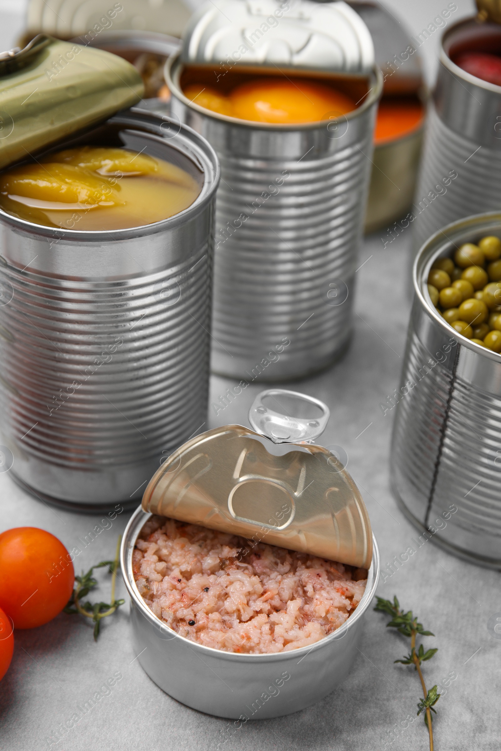 Photo of Open tin cans with different preserved products on grey table, closeup
