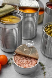 Photo of Open tin cans with different preserved products on grey table, closeup