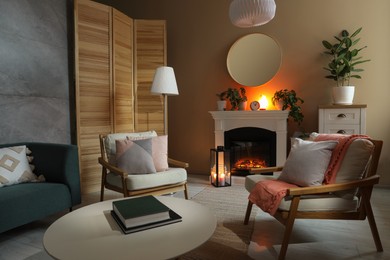 Stylish fireplace near comfortable armchairs and coffee table in cosy living room. Interior design