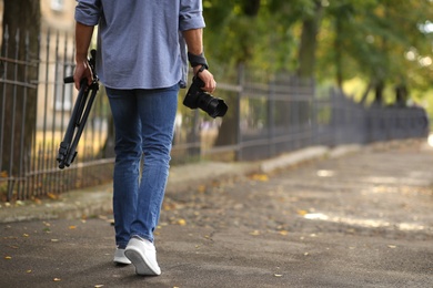 Photographer with professional camera and tripod outdoors, closeup