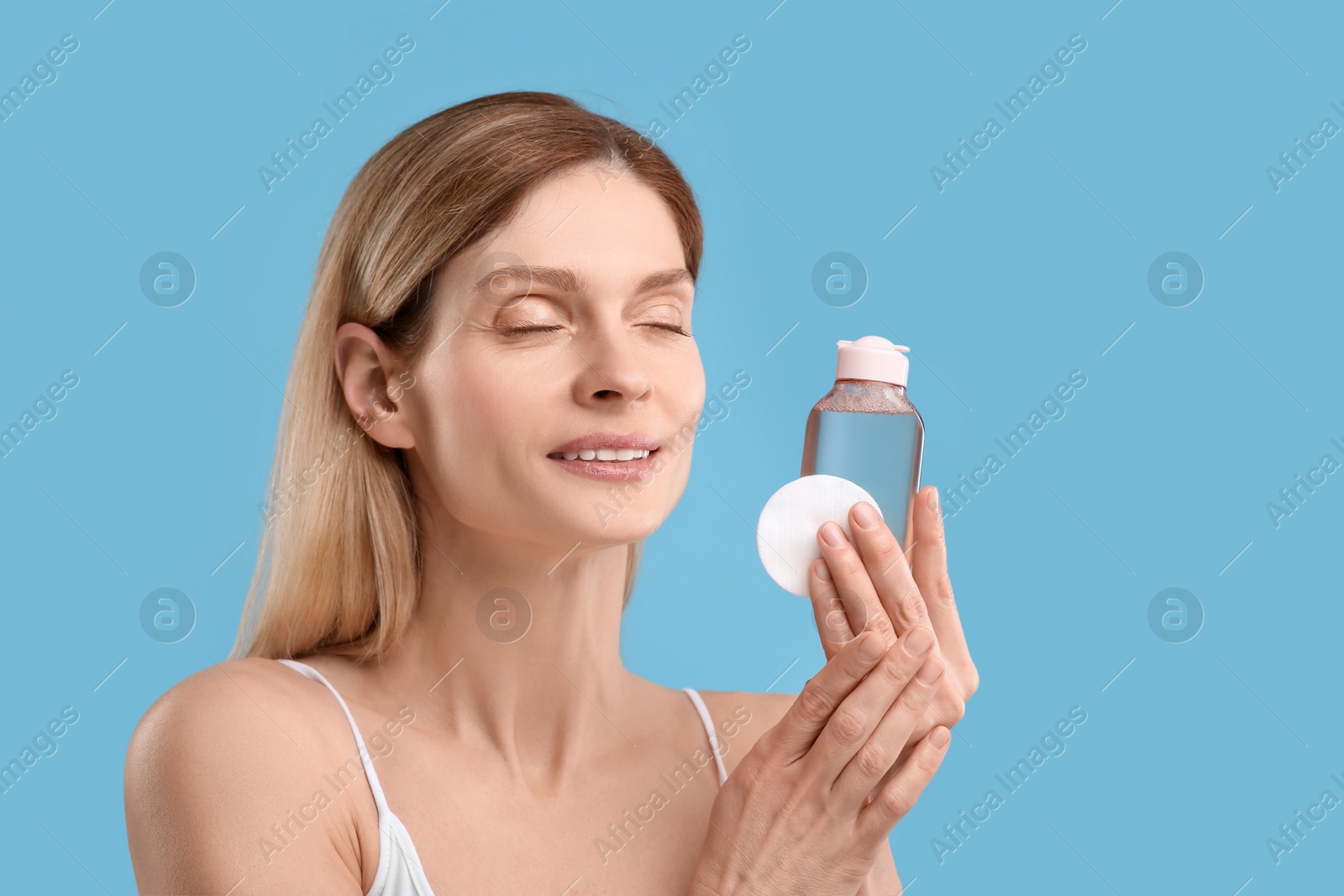 Photo of Beautiful woman with makeup remover and cotton pad on light blue background, space for text