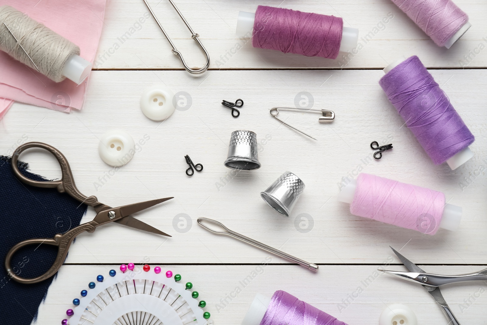 Photo of Flat lay composition with thimbles and different sewing tools on white wooden table