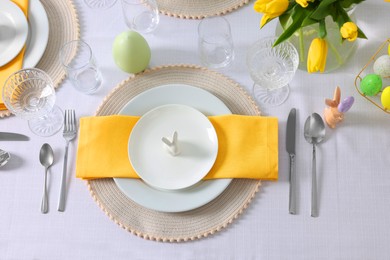 Photo of Festive table setting with glasses, painted eggs and vasetulips. Easter celebration