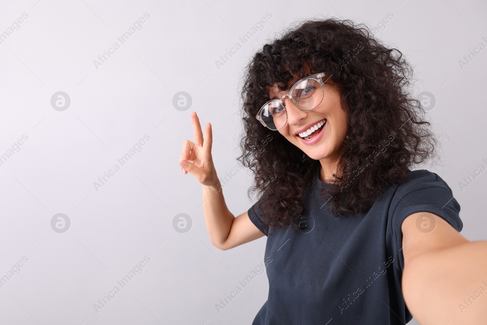 Photo of Beautiful young woman in eyeglasses taking selfie on light grey background