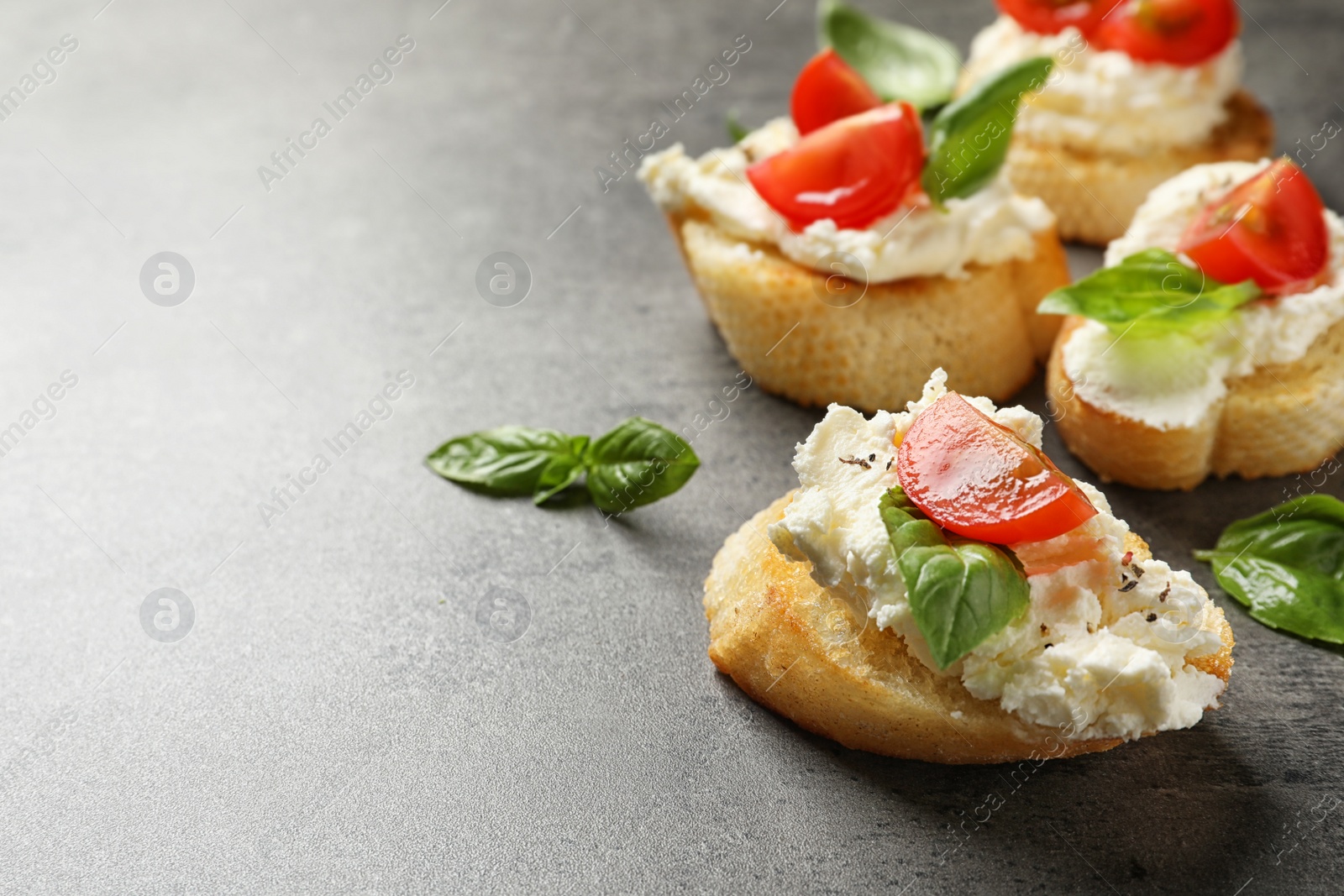 Photo of Pieces of baguette with tasty cream cheese and tomatoes on gray table. Space for text