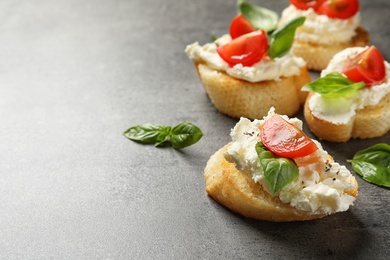 Pieces of baguette with tasty cream cheese and tomatoes on gray table. Space for text