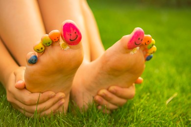 Photo of Teenage girl with chamomiles and smiling faces drawn on toes outdoors, closeup