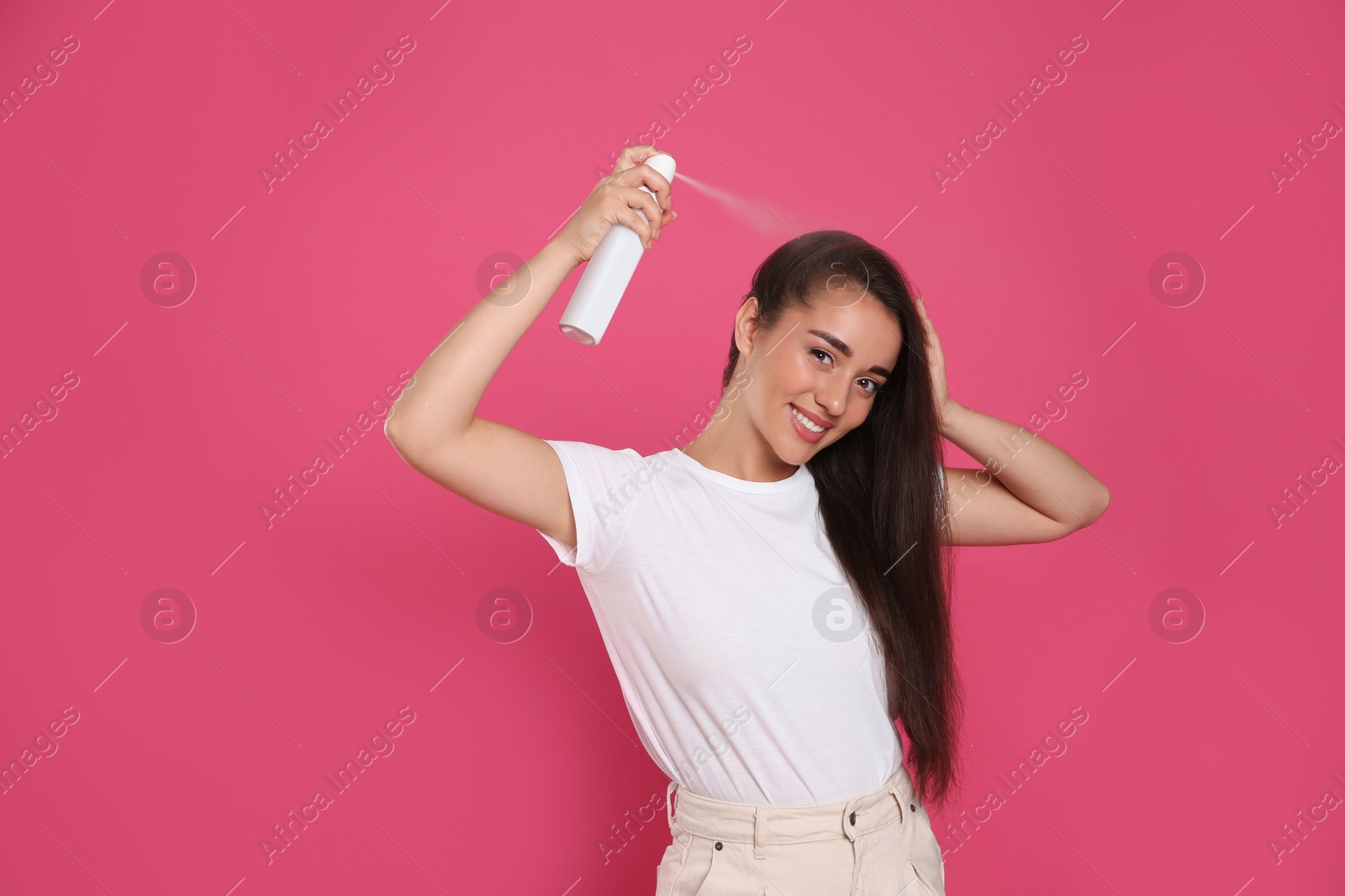 Photo of Young woman applying dry shampoo against pink background