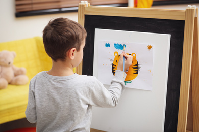 Little child painting on easel in room