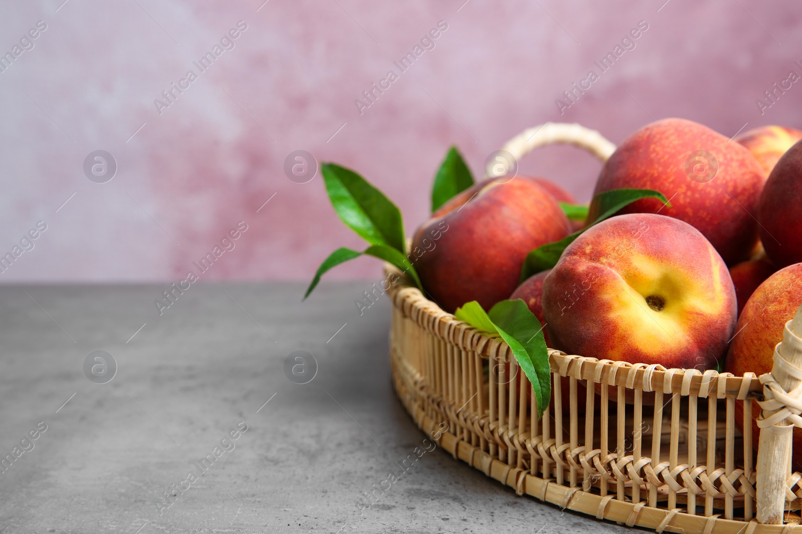 Photo of Wicker tray with tasty peaches on grey table against pink background, space for text