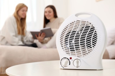 Photo of Women reading book in bedroom, focus on electric fan heater