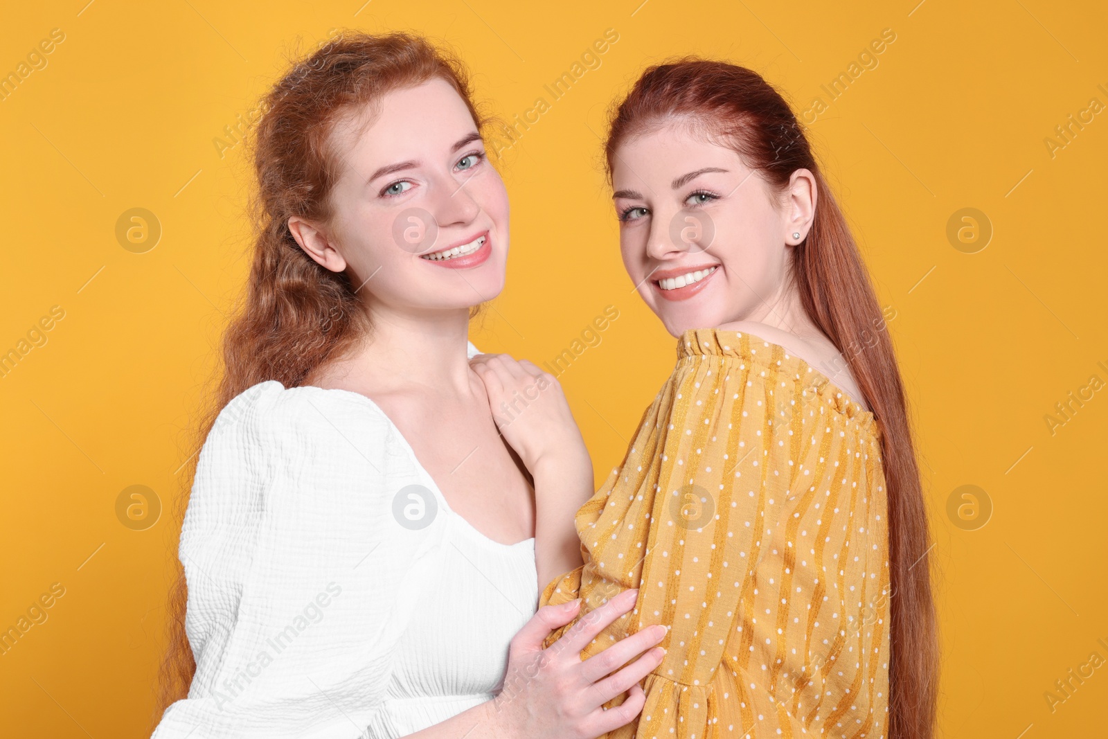 Photo of Portrait of beautiful young redhead sisters on orange background