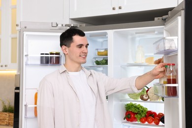 Photo of Happy man taking sauce out of refrigerator in kitchen